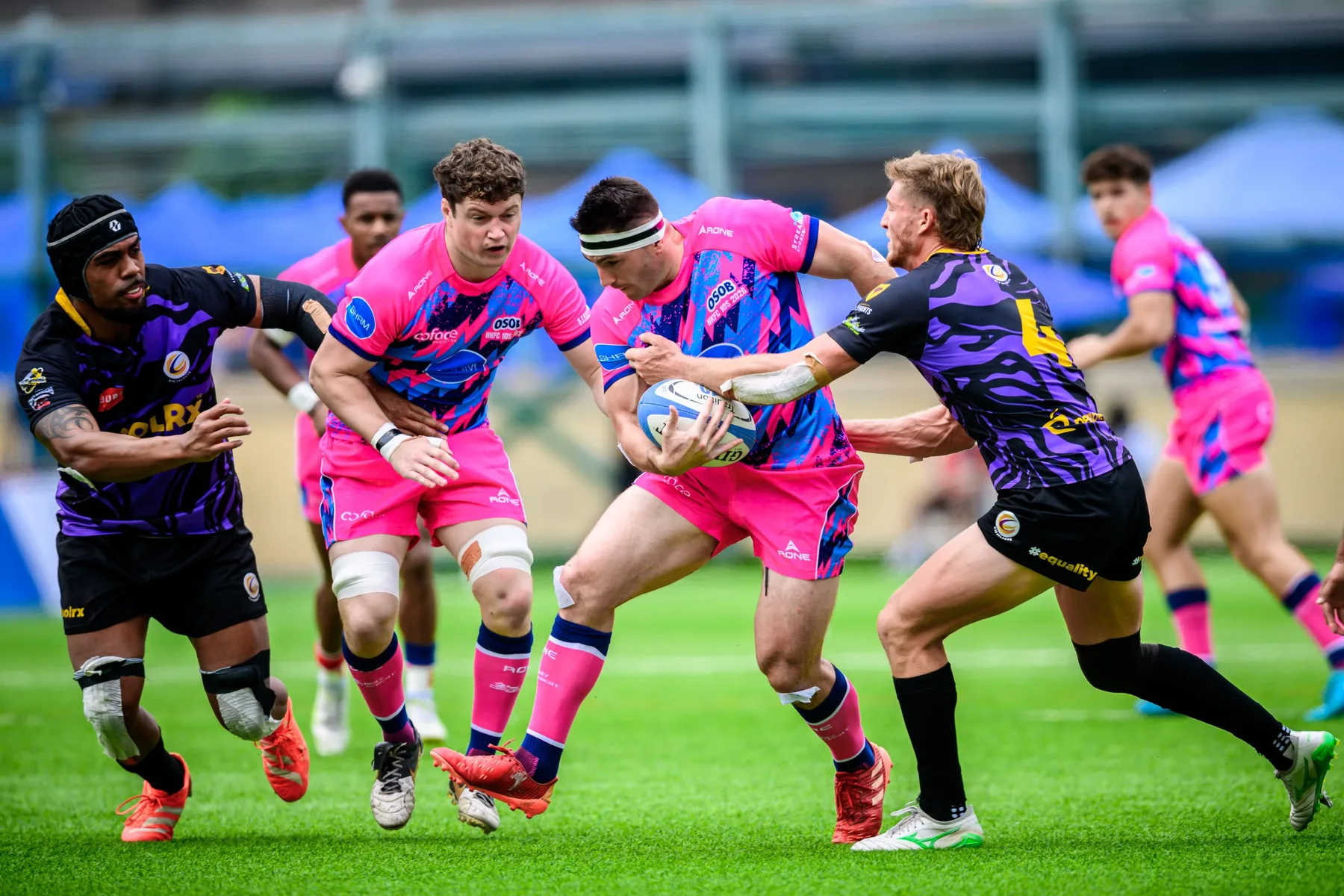 Headbanded OSOB player carries the ball into contact as Tens Selects defenders in purple grab him on both sides
