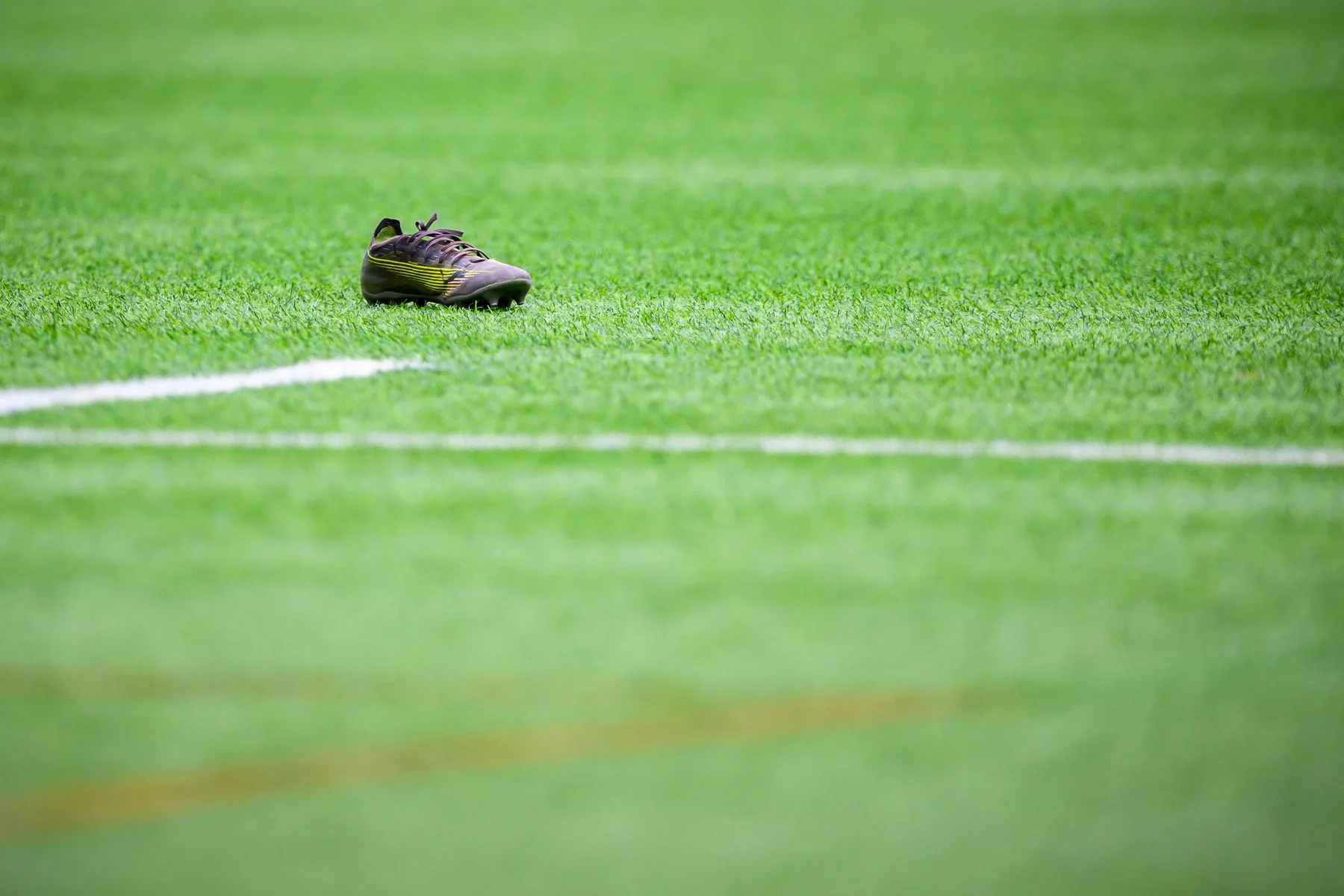 Single rugby boot lies on the artificial turf beside the white pitch lines, with no players in view