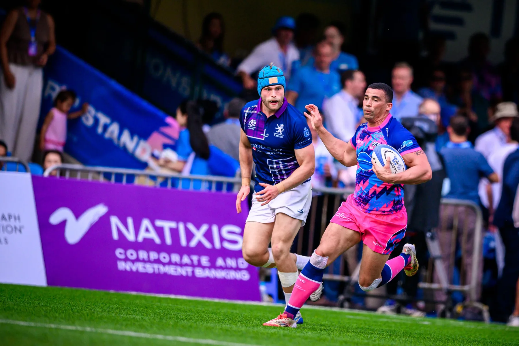 OSOB ball carrier runs the touchline past an Exiles player in a light blue skull cap, Natixis banner behind